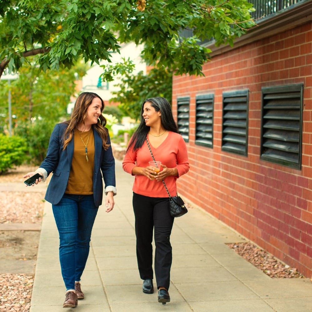 two women walking down a sidewalk talking to each other